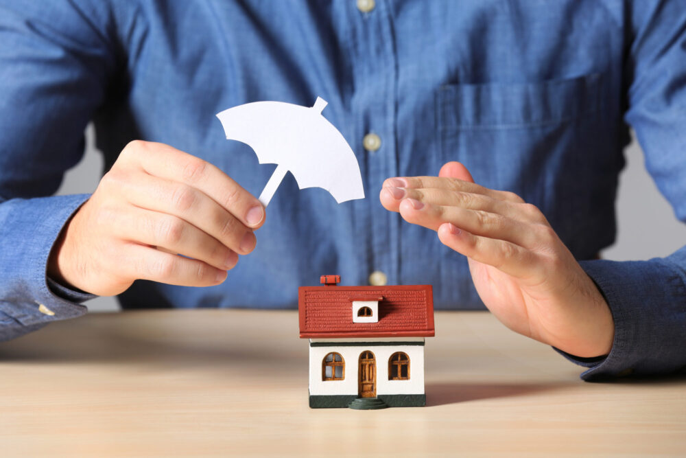 Man holding an umbrella over small house to represent a home warranty